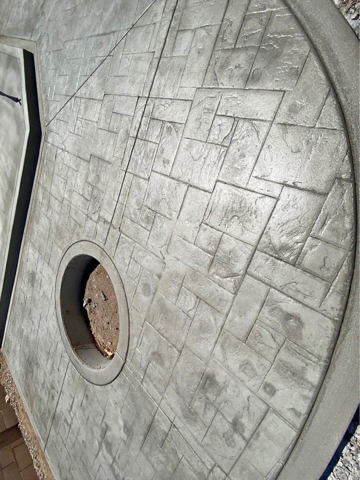 Close-up of a circular outdoor fire pit on a large, textured concrete patio with a decorative pattern. Crafted by Mesa Master Concrete, the contemporary design reflects the expertise of top concrete contractors, making it a standout feature in any space.