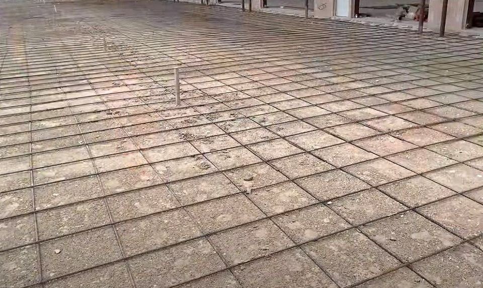 The concrete floor features a grid of exposed steel reinforcement bars at a construction site. Prepared for further work by Mesa Master Concrete, a leader among commercial concrete contractors, some debris is visible on the surface, with structural elements in the background.